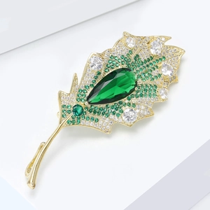 Elegant gold leaf brooch with green zircons and pear-shaped gemstone on white stand