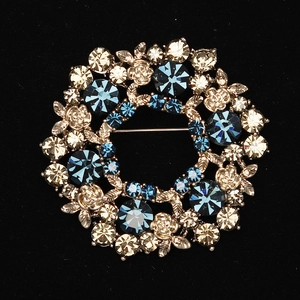 Detail of elegant wreath brooch with navy blue crystals and silver roses on black background