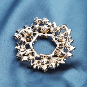 Back view of elegant silver flower brooch with crystal inlay on blue satin background