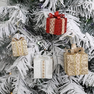 Lace Christmas gift box ornaments in red, gold, and white hanging on a snowy tree