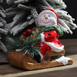 Ceramic snowman figurine on brown wooden sleigh with festive pine and berry decorations