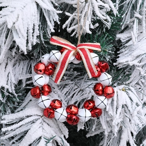 Christmas wreath with red and white bells and a striped bow hanging on a snowy pine branch