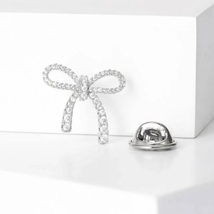 Elegant silver bow brooch with sparkling pavé zircons on a white geometric stand