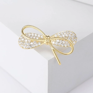 Broche nœud exquise plaqué or sertie de zircons brillants sur un socle blanc épuré