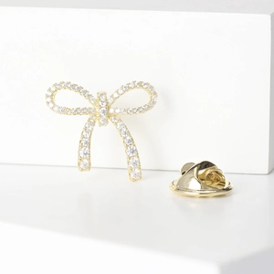 Elegant gold bow brooch with white crystals on a white minimalist stone display
