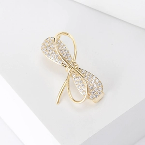 Détail macro d'une broche nœud dorée avec zircons pavés sur un socle blanc