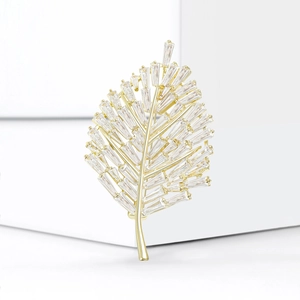 Close-up of golden leaf brooch with channel-set baguette zircons on minimalist background