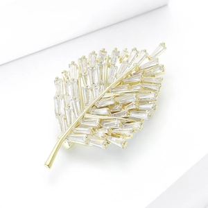 Detail shot of golden leaf brooch with sparkling baguette cut zircons on white background
