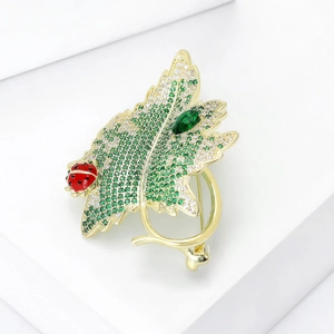 Detailed close-up of leaf brooch with green zircons and ladybug on white stand