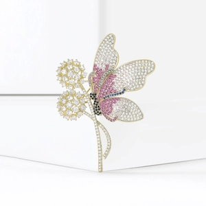 Spilla dorata a farfalla e dente di leone con strass multicolori su supporto bianco