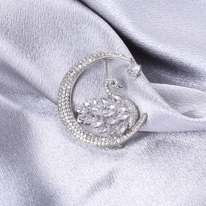 Macro view of crystal swan and crescent moon brooch with shimmering drop pendant