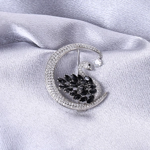 Macro shot of silver crescent moon and black swan brooch with zircon on silk fabric