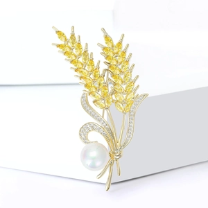 Elegant gold wheat brooch with yellow crystals and a lustrous round pearl on white podium