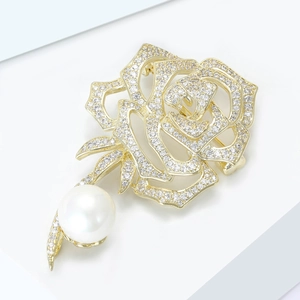 Gros plan d'une broche rose dorée avec pavé de zircons et perle d'eau douce blanche