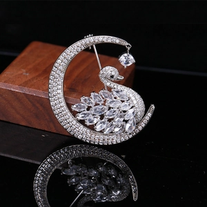 Detailed macro shot of a crystal moon and swan brooch on a dark reflective surface