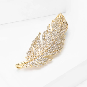 Vue détaillée d'une broche plume dorée sertie de zircons brillants sur support blanc