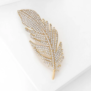 Détail de la broche plume sertie de zircons brillants sur un support géométrique blanc