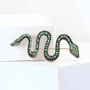 Macro detail of snake brooch featuring green rhinestones and antique gold finish