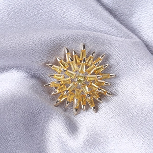 Elegant gold snowflake brooch with yellow zircon crystals on silver silk background