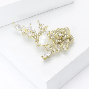 Détail d'une broche fleur dorée avec une grande perle blanche et des zircons brillants