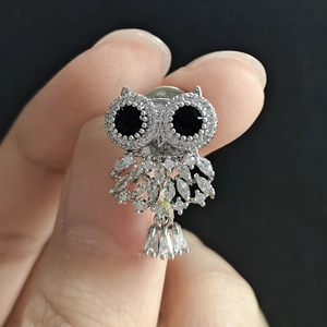 Macro shot of silver owl brooch with white zircon stones and black gemstone eyes