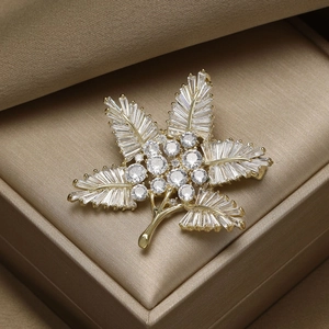 Detailed macro view of a golden maple leaf brooch with sparkling zircon in a luxury jewelry box