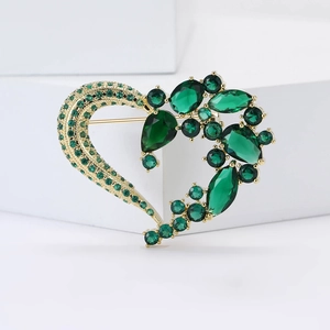 Dettaglio di un'elegante spilla a cuore in oro con zirconi verde scuro su cubi bianchi