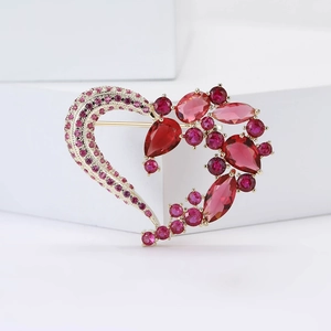 Dettaglio macro di elegante spilla a cuore con cristalli rossi e rosa su base dorata