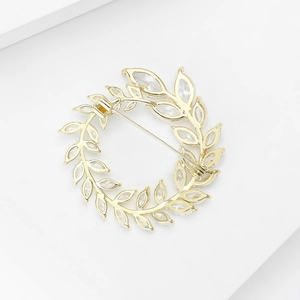 Makro-Detail der goldenen Olivenzweig-Brosche mit der sicheren Metall-Anstecknadel-Rückseite