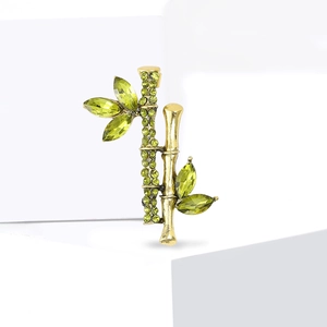 Elegant bamboo brooch with green crystals and gold plated metal on white background