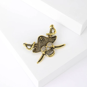 Detailed close-up of retro gold pirate skull brooch with crossed swords and embossed texture