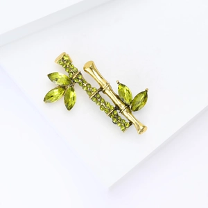 Bamboo shaped vintage brooch with olive green crystals on a minimalist white platform