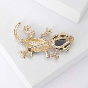 Vintage gold lizard brooch with black gemstone and crystal accents on a white stone base
