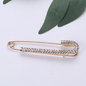 Dettaglio di una spilla da balia dorata con strass bianchi brillanti su sfondo grigio