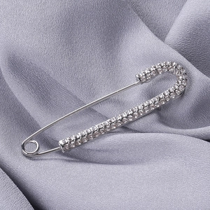 Dettaglio di una grande spilla da balia argentata con strass su tessuto satinato
