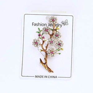 Detailed macro view of gold flower brooch with pink rhinestones and colorful enamel leaf