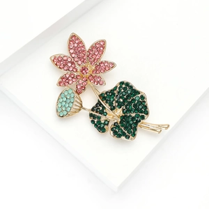 Elegante lotusbloem broche met roze strassteentjes en groene bladeren op wit dienblad
