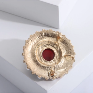 Vintage Baroque sunburst brooch with red ruby center and pearls on a white podium