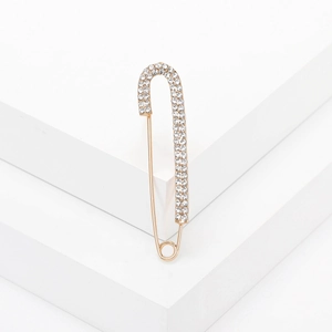 Elegante spilla a balia dorata con strass bianchi brillanti su piattaforma bianca