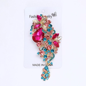 Detailed macro view of gold-plated pin brooch with pink teardrop crystal and colorful rhinestones