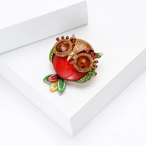 Detail of colorful owl brooch with red enamel body and green crystal wings on white stand