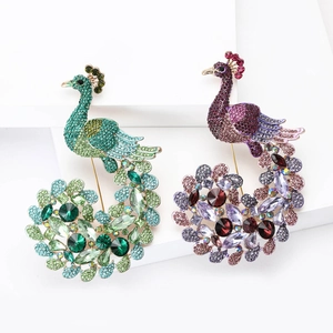 Exquisite peacock brooches with sparkling crystals in green and purple on a white stand