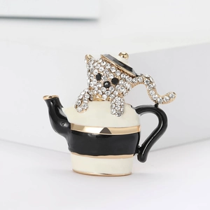 Détail d'une broche chat en théière en émail avec des strass brillants sur support gris
