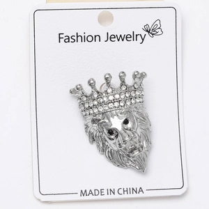 Detailed close-up of a silver lion head brooch with a crystal crown on white card