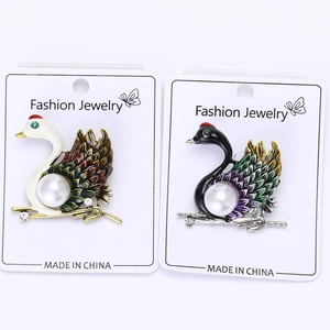 Detail of swan brooches featuring colorful enamel drip wings and elegant white pearls