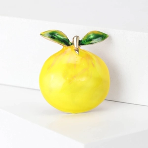Macro shot of vibrant yellow enamel lemon brooch with green leaves on white stand