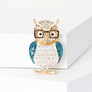 Sparkling owl brooch with blue wings and glasses, set on a white platform base
