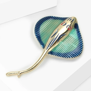Macro shot of a golden stingray brooch with blue-green enamel fins and red eye detail
