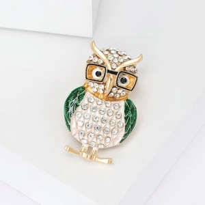 Detail of owl brooch with white rhinestones and green enamel on a golden metal base