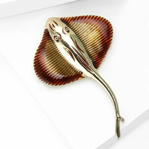 Detailed close-up of golden stingray brooch with reddish-brown enamel on a white podium